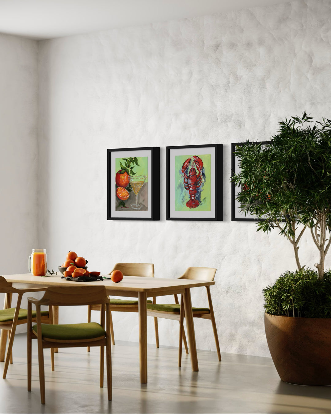 Three paintings hung as a gallery wall in a dining room on a bright white wall with a green tree. The first painting is of an orange and a half with an orange martini in a glass, the second is a red lobster and the third is of more bright oranges. All are painted onto lime green backgrounds and framed in modern black frames