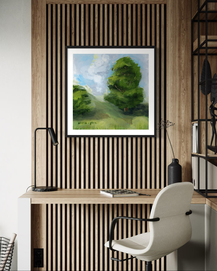 A framed, ready to hang giclee print of green trees and rolling hills with blue sky and white clouds. From an original painting from Arden Upton's Blue Skies Collection. Styled above a desk. Great for decorating living room, bedroom and hallway walls in your home and gifting