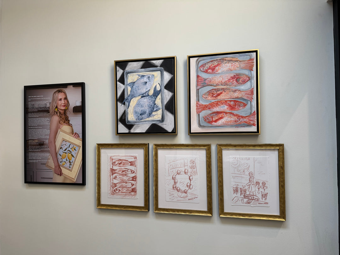 Gallery wall of Arden Upton's Frank's Table Collection featuring five of her paintings and sketches and a photo of her with her biography. The Oil Paintings are of two blue fish on a platter on a black and white table and of five red fish on. pan on a white background. The three sketches are of five red fish, eggs on an egg stand on a table, and people sitting at a table with  server and tables with place settings. Perfect for Gathering spaces, gallery walls and kitchens