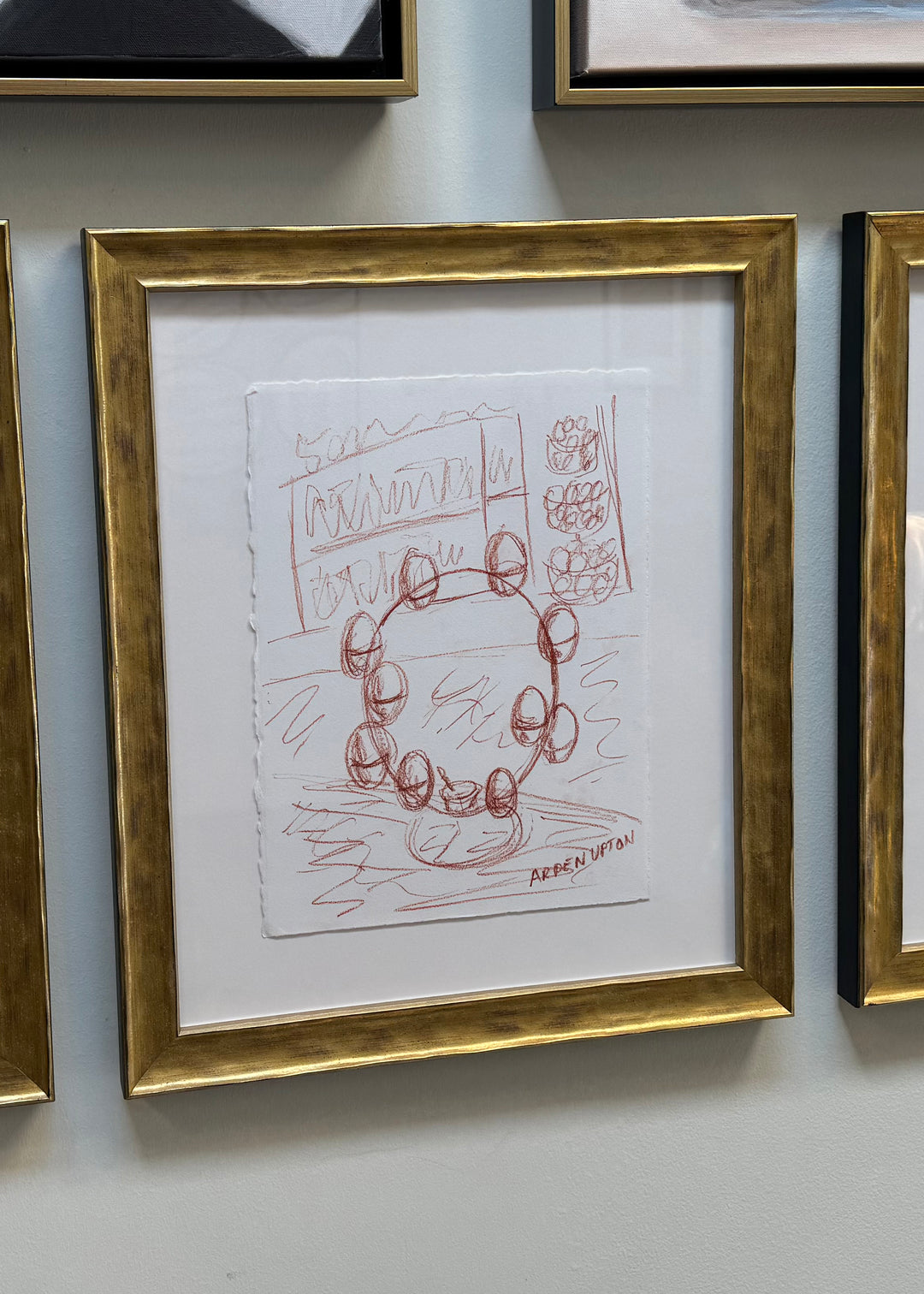 A sketch from Arden Upton's Frank's Table collection depicting farm fresh eggs sitting on the counter top in an egg stand before the ingredients are turned into art. The sketch is matted and framed in a textured gold frame. 