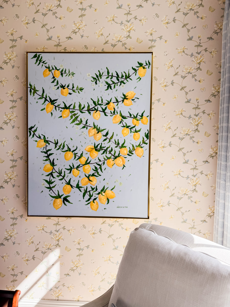 Original Painting by Southern Artist Arden Upton on Lemon tree branches bursting with lemons and green leaves on a light blue background. It is hung in a bedroom with soft wallpaper featuring yellow flowers. Would also be perfect for kitchens, dining areas, and other places in your home. 