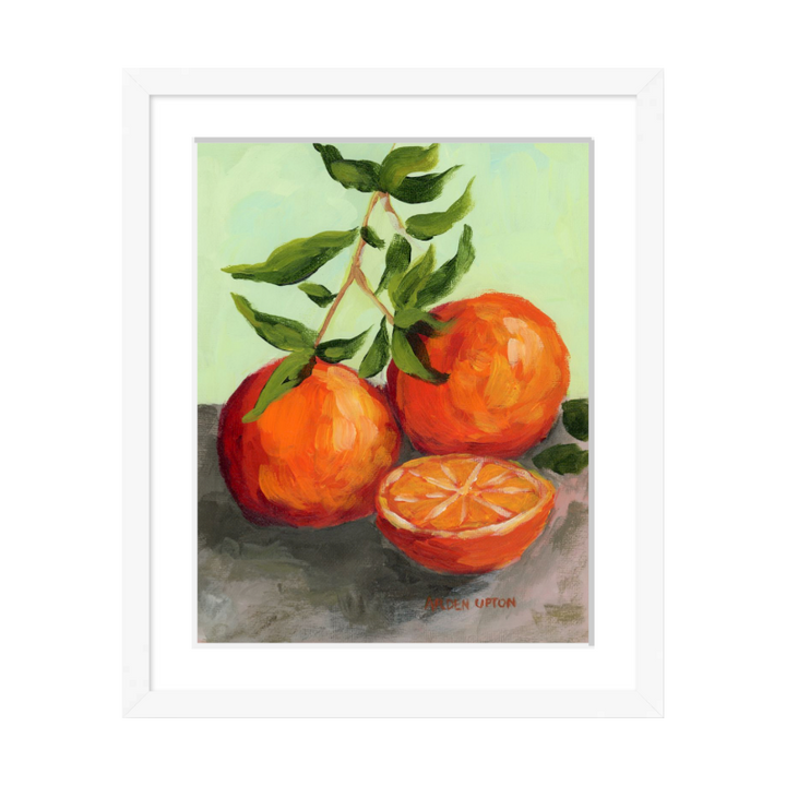 Culinary wall art – Orange Still Life framed painting by Arden Upton, ideal for kitchen and dining room décor. Painting shows teo and a half oranges on a green leaf-covered stem on a grey surface with a lime green background