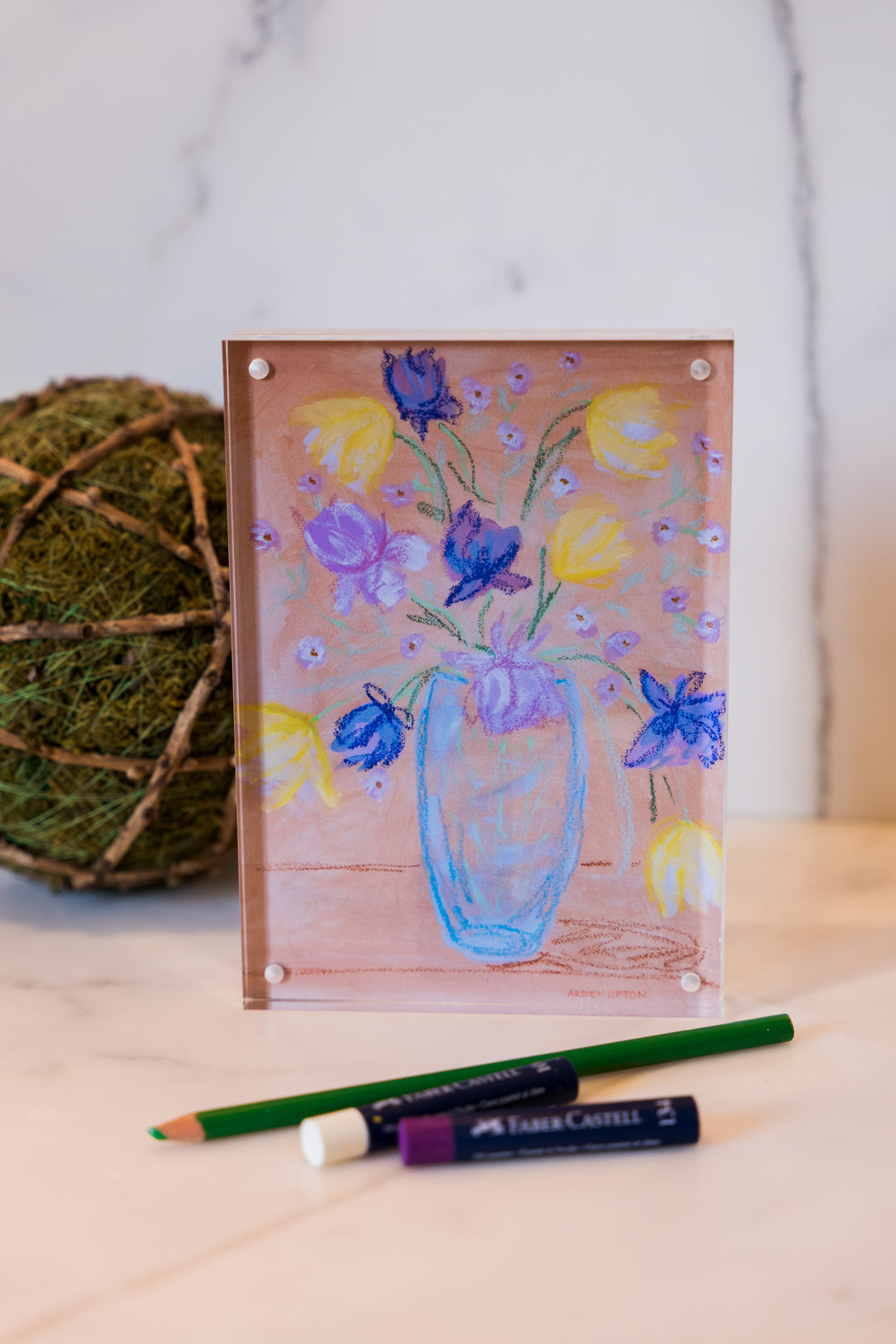 Purple and yellow flowers in a blue vase on a peach background with green leaves from Arden Upton's Flowers that Last Collection  Framed in an acrylic block and staged with art supplies and greenery. These make great teachers gifts and hostess gifts and are beautiful. 