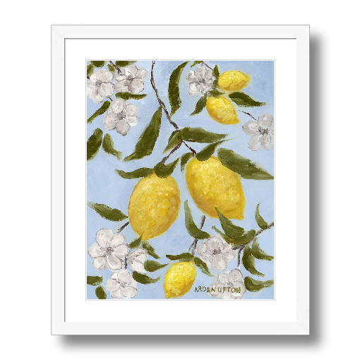 A framed art print featuring a painting from Arden Upton's Lemonade Collection of lemons , leaves and white floral elements against a blue background, with a white mat and black frame.