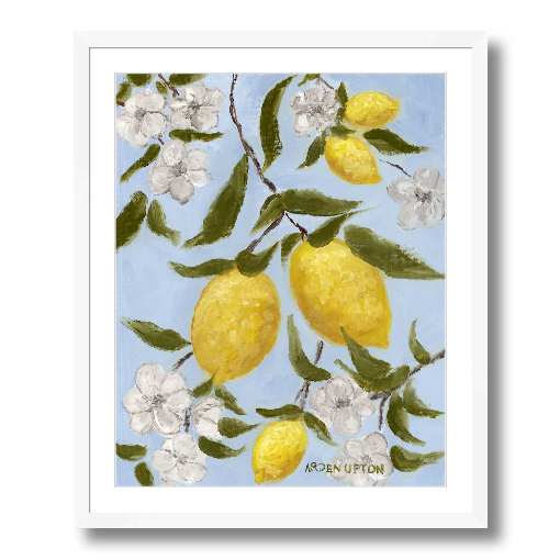 A framed art print featuring a painting from Arden Upton's Lemonade Collection of lemons , leaves and white floral elements against a blue background, with a white mat and black frame.
